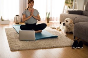 woman meditating with laptop and dog in living room