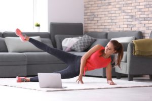 woman doing leg lifts in living room with laptop computer